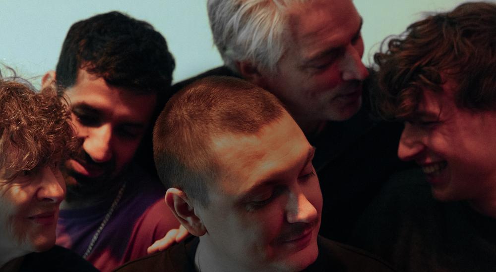 Louis surrounded by the cast, all with their eyes closed