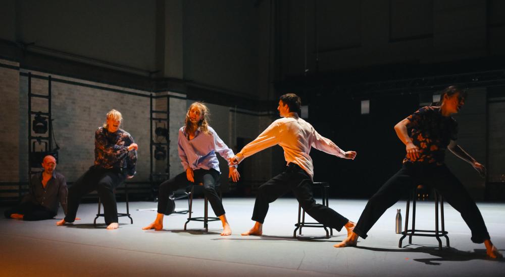4 dancers moving on chairs, 1 lying on the floor