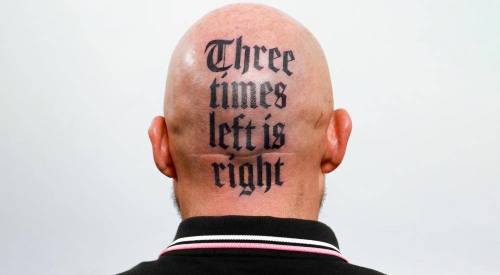 The back of bald person's head with a tattoo that reads "Three times left is right"