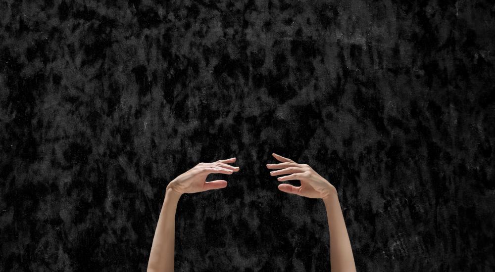 Two hands in a ballet pose in front of a black background