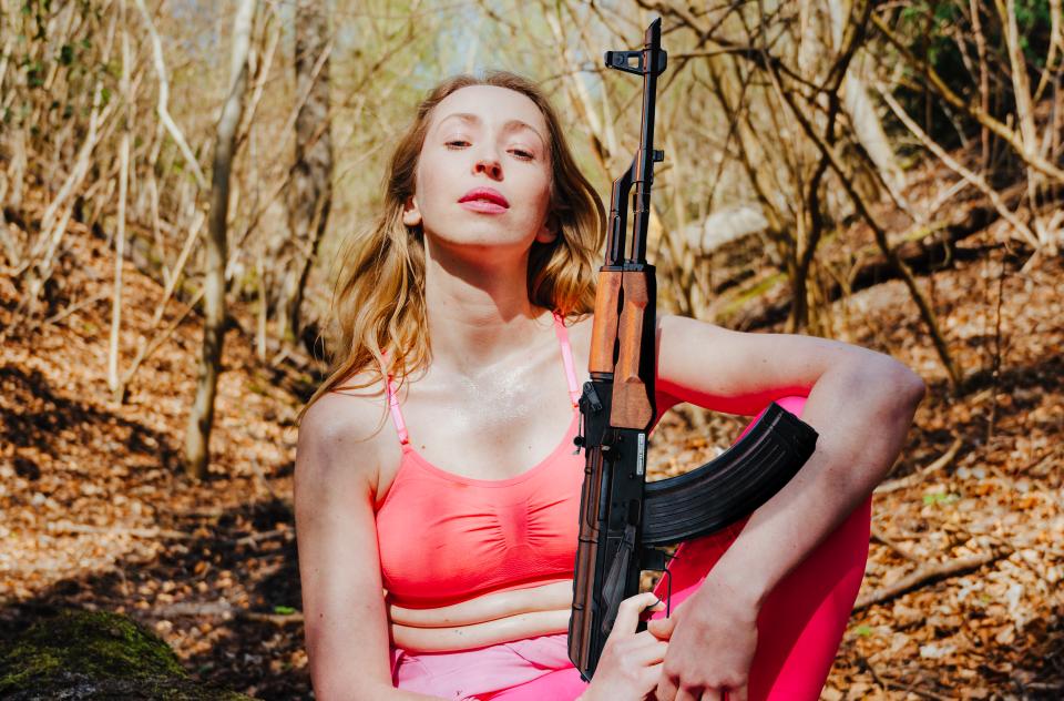 A blonde woman in yoga clothes holding an automatic rifle