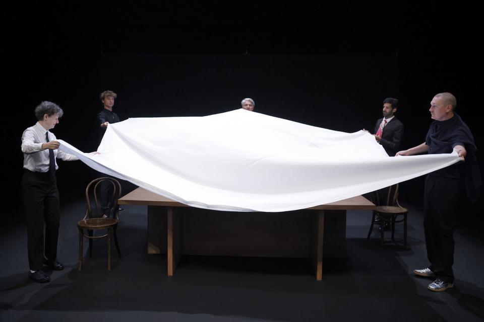 Five actors pulling a white tablecloth over a table