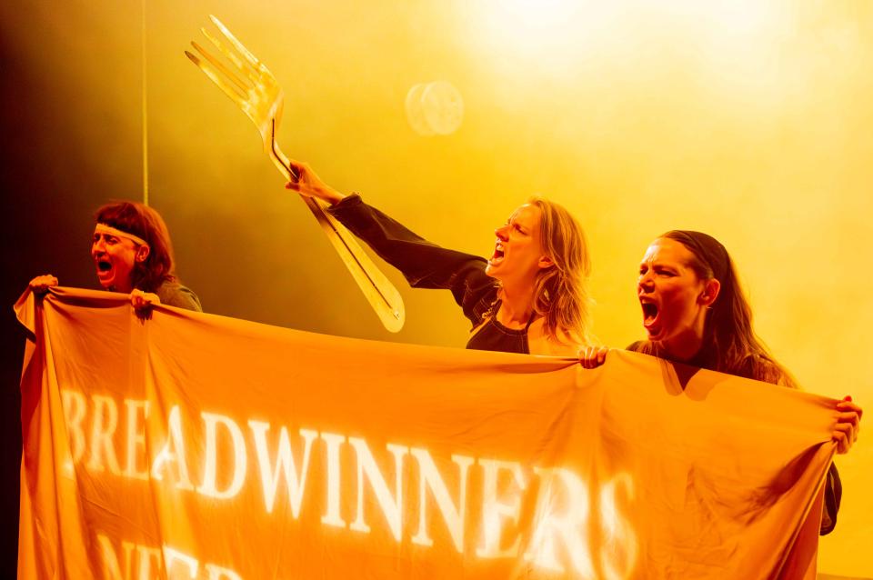 Three women holding a banner, the top of which reads BREADWINNERS, with one of them also holding a huge fork in one hand