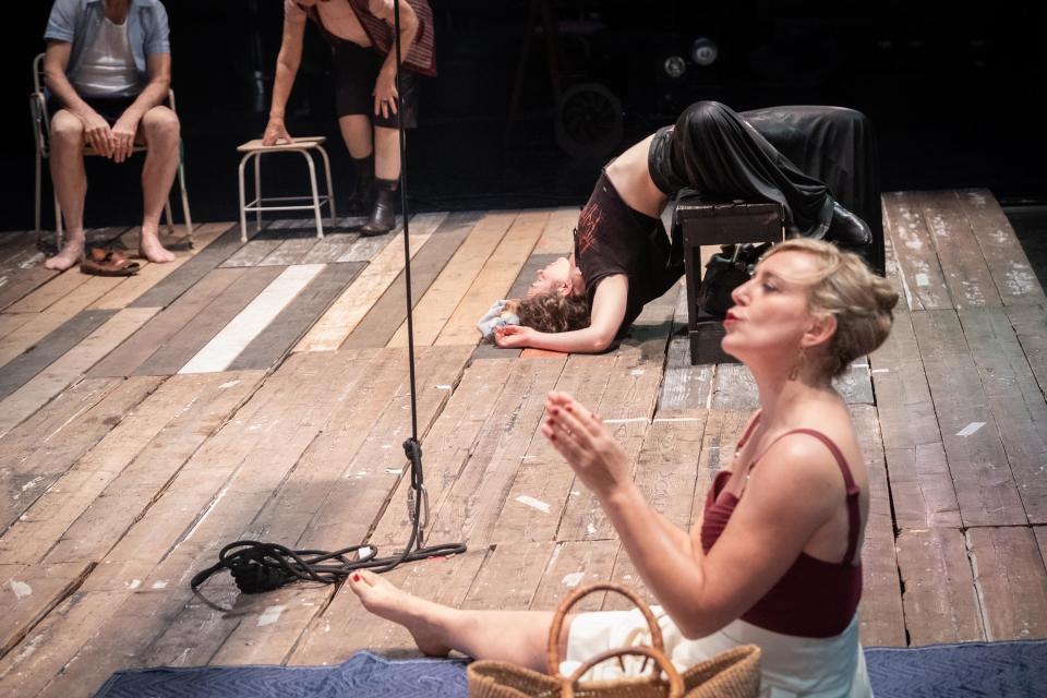 Someone sitting on a mat on a wooden floor, with someone else lying on a stool behind them