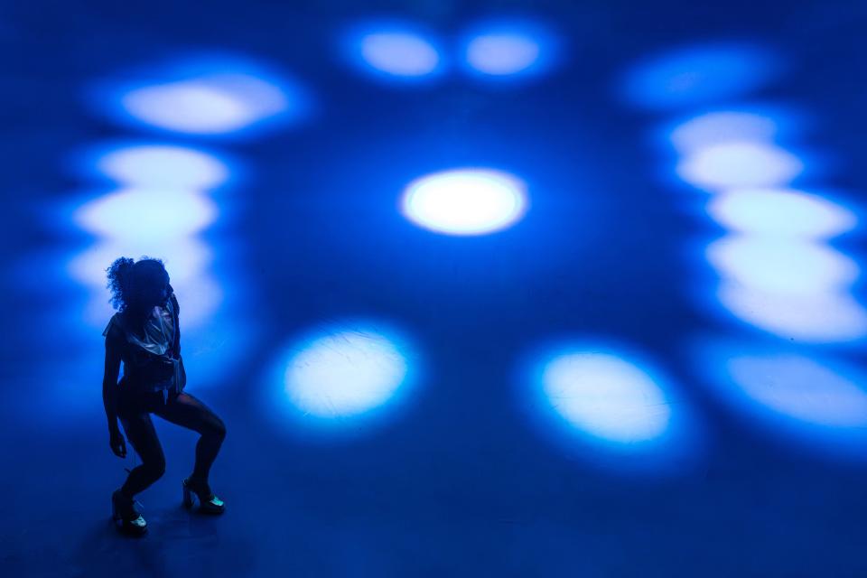 1 performer with black clothes dancing on a bright blue floor